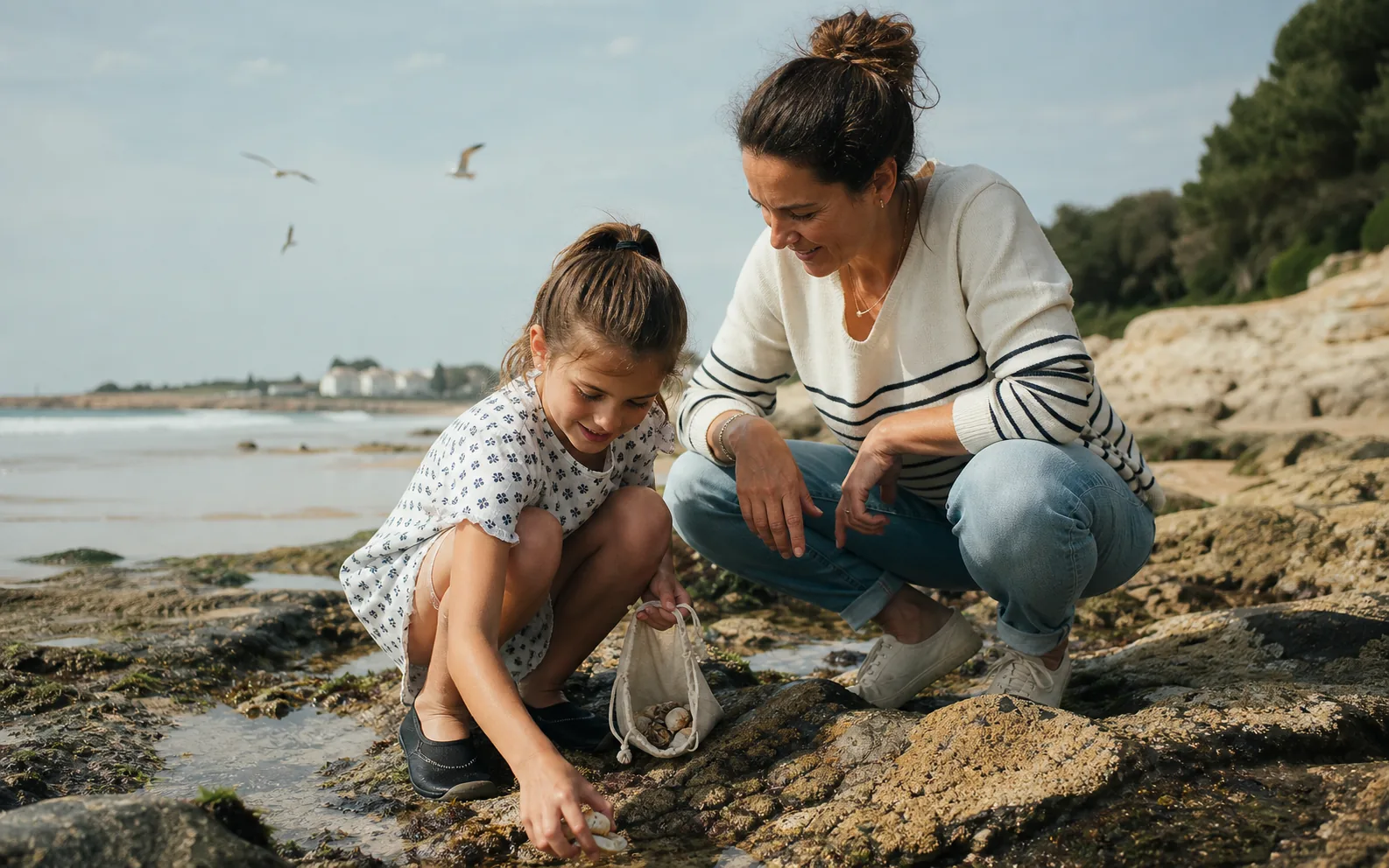 Mutter und Tochter entdecken gemeinsam Muscheln an einem sonnigen Strand.