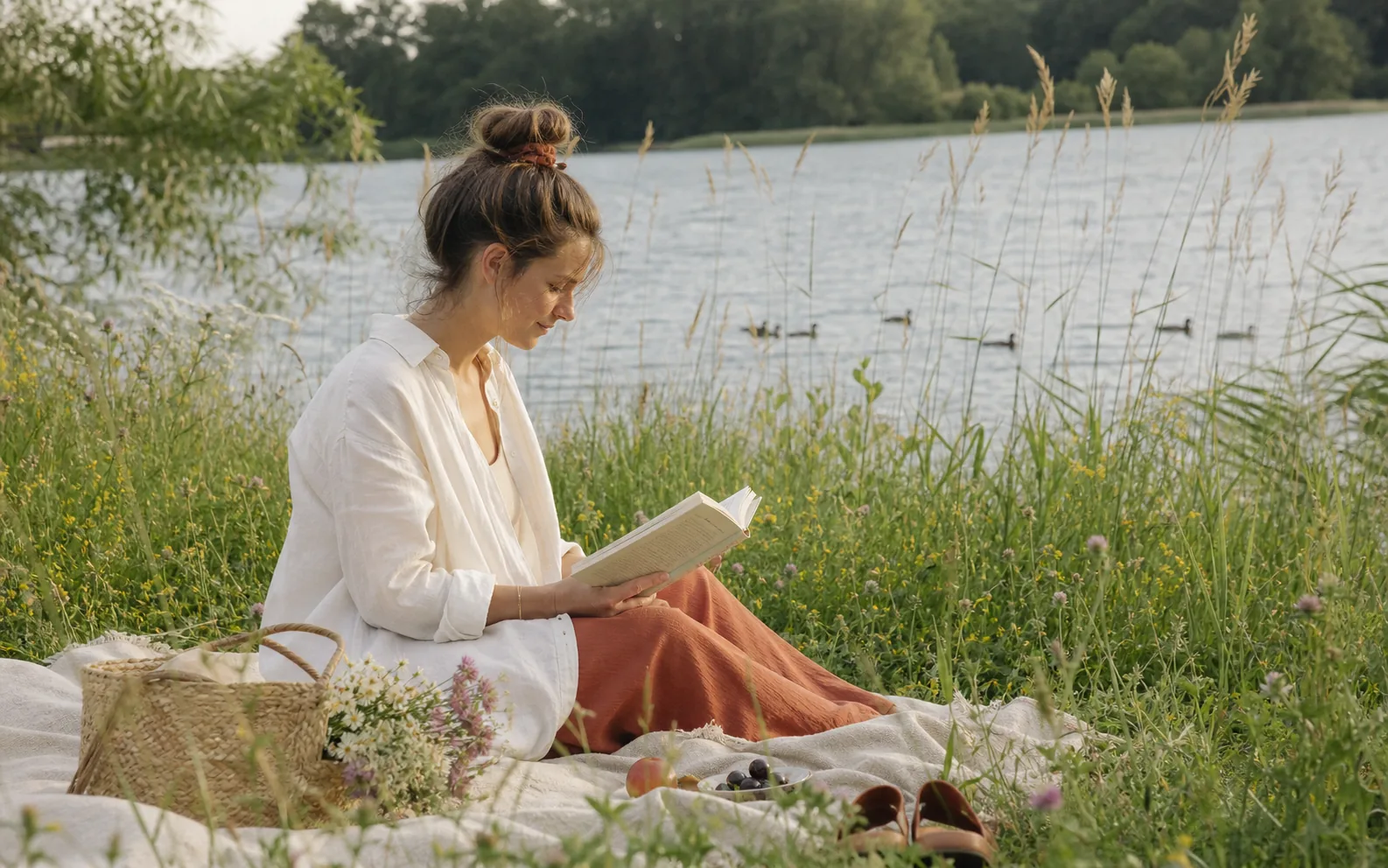 Eine Frau liest entspannt auf einer Blumenwiese am See.